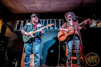 two men playing guitars in front of a sign